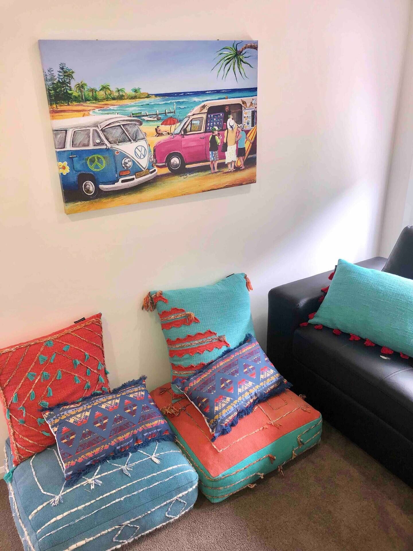 Sala de estar com uma pintura de tema praiano, almofadas coloridas e um sofá de couro preto.