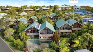 A cluster of modern villas with green roofs, surrounded by lush greenery and palm trees.