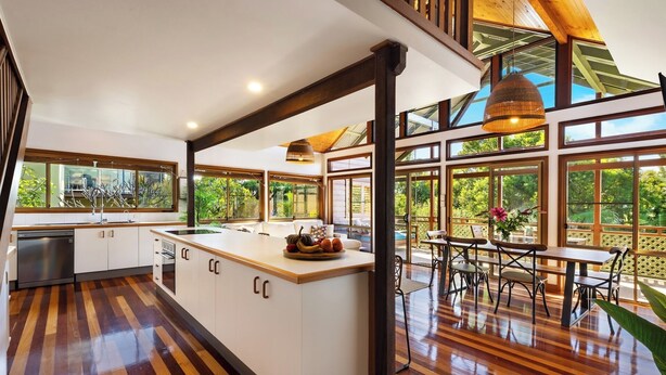 A spacious kitchen with a large island, wooden flooring, and large windows offering a view of the outdoors.