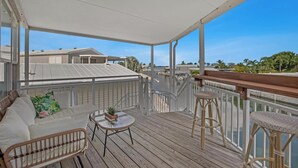 Eine überdachte Terrasse mit einer weißen Couch, einem kleinen runden Tisch und zwei Korbstühlen.