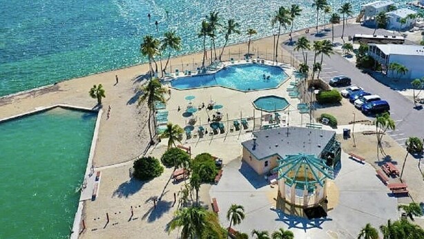 Eine Vogelperspektive eines Resorts mit großem Pool, Palmen und einem Strandbereich.