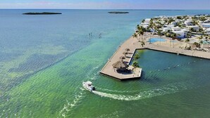 Eine Luftaufnahme einer Insel mit einem Resort, einem Anlegesteg, einem Pool und einem Strandabschnitt mit Sonnenschirmen.