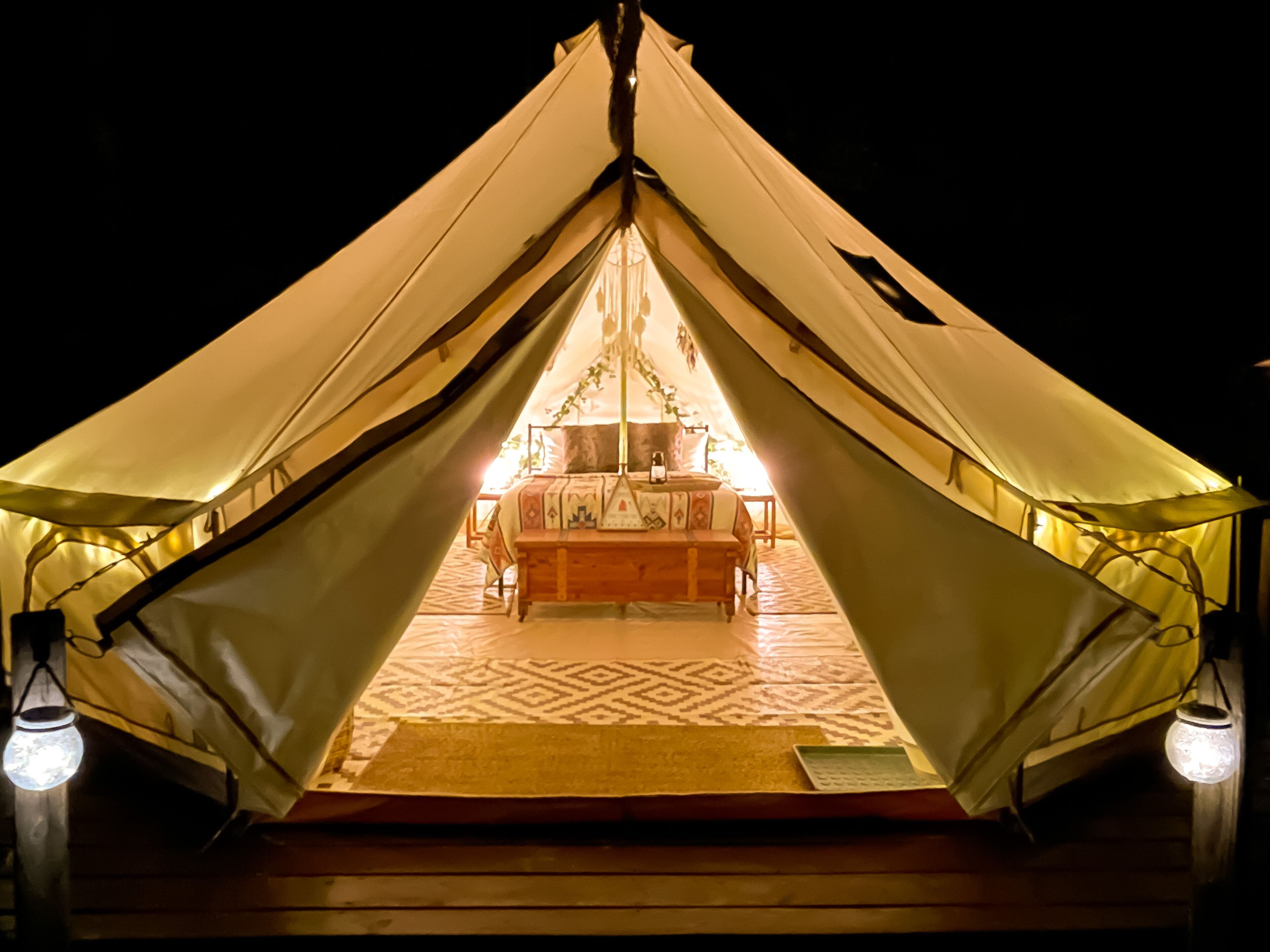 A tent with a bed and a table in the center, surrounded by a patterned floor.