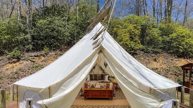 A tent with a bed inside, surrounded by a wooden deck and a patterned rug. - 4200ft Luxury Stargazing Glamping Haven, Ultra-Private, Near BRP (Maggie Valley)