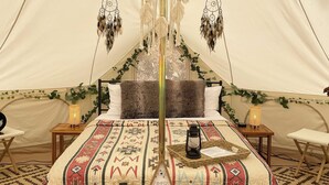A tent with a bed, a hanging dreamcatcher, and a wooden bench. - 4200ft Luxury Stargazing Glamping Haven, Ultra-Private, Near BRP (Maggie Valley)