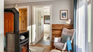 A modern living room with a wood-burning stove, a comfortable armchair, and a view through an open door to a balcony. - Apartment "Alpenrose" with Mountain View, Shared Terrace & Wi-Fi (Leutasch)