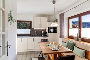 A compact kitchen with white cabinets, a dining table with a bench, and a view of the outdoors through a window.