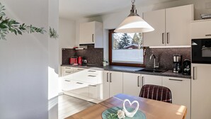 A modern kitchen with white cabinets, a dining table with a heart-shaped centerpiece, and a hanging pendant light. - Apartment "Alpenrose" with Mountain View, Shared Terrace & Wi-Fi (Leutasch)