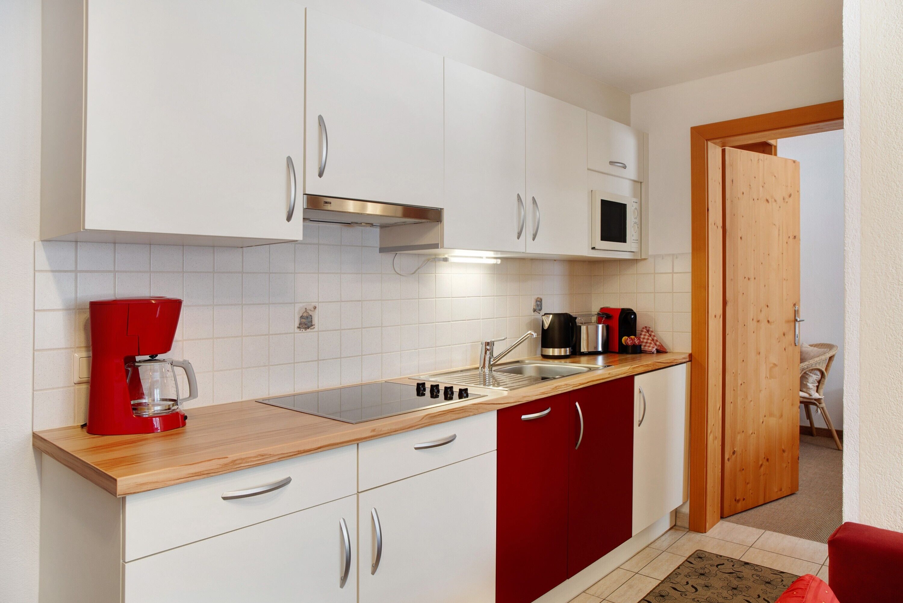 Una cucina moderna con pensili bianchi, un piano di lavoro rosso, una macchina del caffè, un bollitore e un forno a microonde.