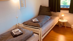 Una habitación pequeña y acogedora con dos literas, una mesita de noche con lámpara, y una ventana con cortinas.