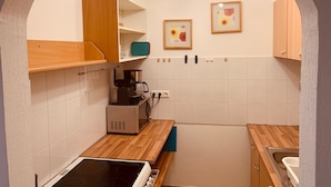 Una cocina con paredes de azulejos blancos, armarios de madera, microondas, cafetera y estufa.