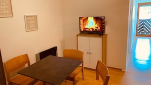 Una habitación con televisión sobre un mueble bajo, una mesa, dos sillas y un armario.