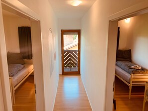Kapea käytävä, jonka molemmilla puolilla on yksi sänky, lattia on puuta ja ovessa on geometrinen kuvio.