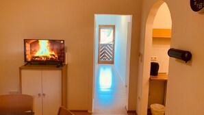 Una sala de estar con chimenea, televisor, comedor y un pasillo que conduce a una puerta con diseño geométrico.