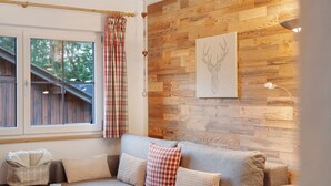 Ein gemütliches Zimmer mit Holzwand, einer Couch mit Kissen, einem Fenster mit Vorhängen und einem gerahmten Bild.