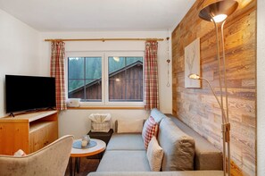 A cozy room with a sofa, a television, a wooden wall, and a window with curtains.