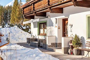 A chalet with a wooden balcony, a snow-covered ground, and a small Christmas tree.