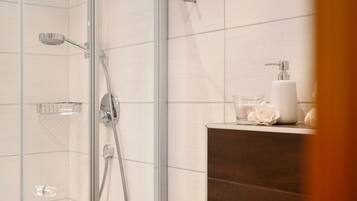 Eine Dusche mit Glastür, einer Glasbrause und einem Seifenspender an der Wand.
