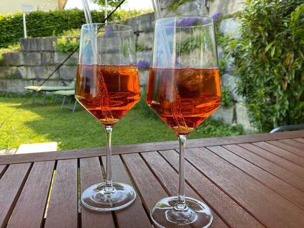 Deux verres d’une boisson rouge sont posés sur une table en bois, à l’extérieur.