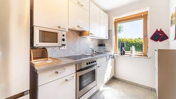 A modern kitchen with white cabinets, a built-in microwave, a stove, and a window with a view of greenery.
