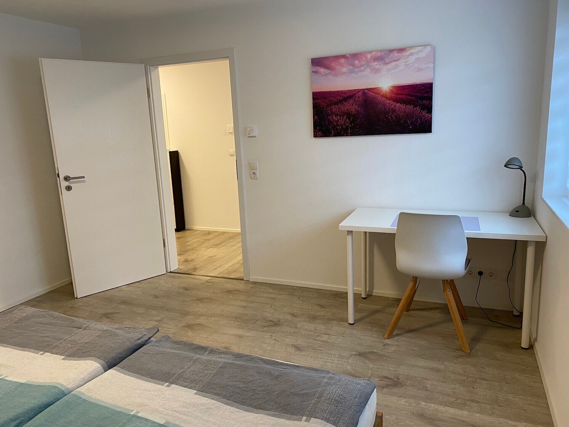 A bedroom with a bed, a desk, and a chair. There is a door leading to another room.