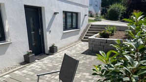 A patio with a chair, a white building with a dark door, and a small garden area. - Apartment 'Alina' with Private Terrace and Wi-Fi (Sinsheim)