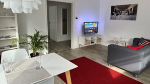A modern living room with a flat-screen TV, a dining table with chairs, a red rug, and a grey sofa. - Apartment 'Alina' with Private Terrace and Wi-Fi (Sinsheim)