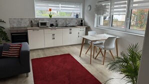 A modern kitchen with white cabinets, a dining area with a table and chairs, a red rug, and a potted plant. - Apartment 'Alina' with Private Terrace and Wi-Fi (Sinsheim)
