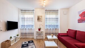 A modern living room with a red sofa, a flat-screen TV, a small white table, a white console table with a potted plant, and a star-patterned rug.