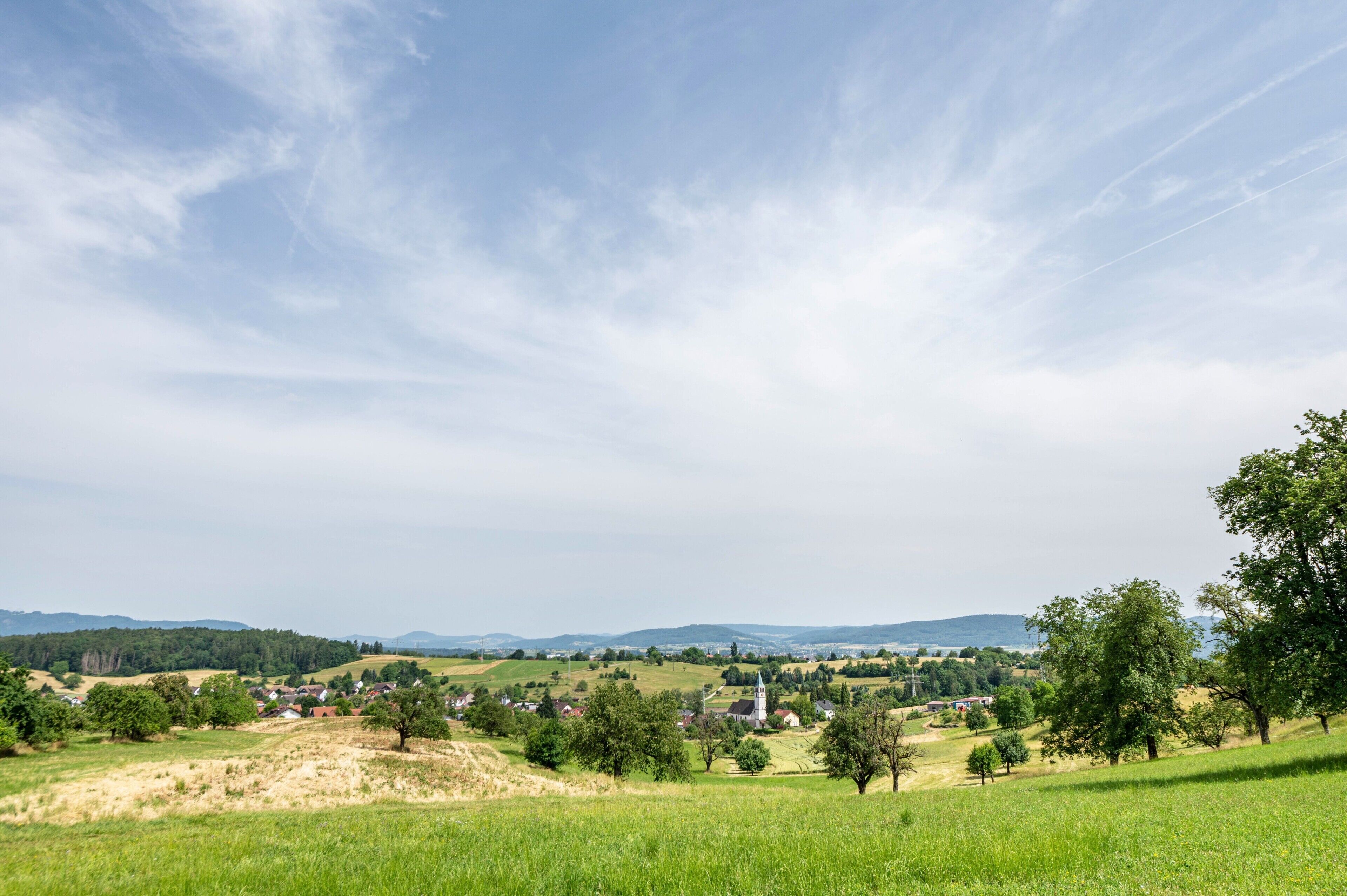 A rural landscape with rolling hills, a church, and scattered houses.