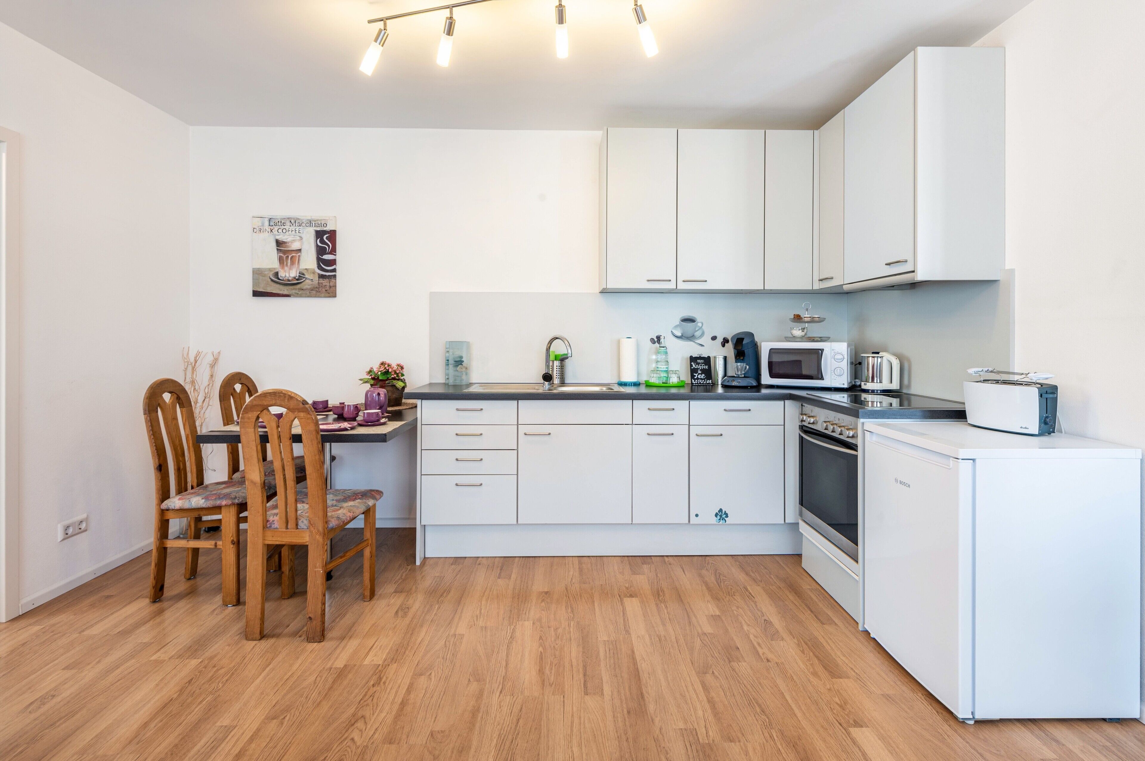Une cuisine moderne avec des meubles blancs, un réfrigérateur Bosch, un four à micro-ondes et un grille-pain.