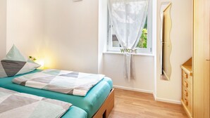 A bedroom with a bed, a window with a curtain, a mirror, and a wardrobe.