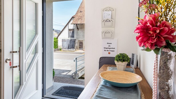 A hotel room entrance with a door, a view of the street, a wall-mounted sign, a small plant, and a decorative vase.