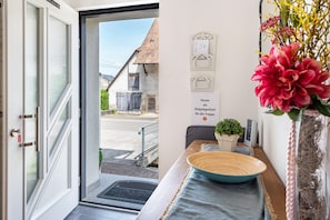 Entrada de una habitación de hotel con una puerta, vista a la calle, un letrero en la pared, una planta pequeña y un jarrón decorativo.
