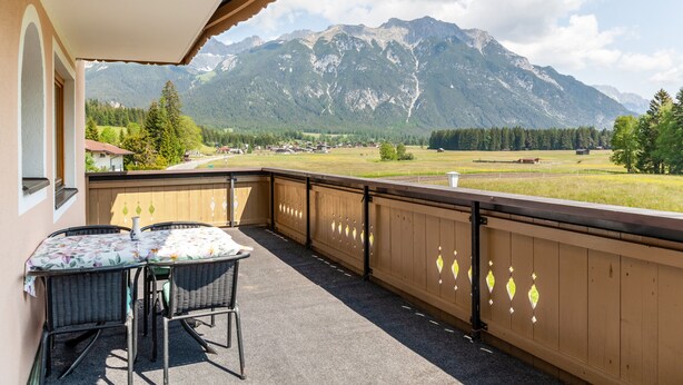 Un balcon avec une table et des chaises, une vue sur les montagnes et une clôture en bois.