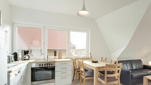 A modern kitchen with a dining area, including a stove, oven, and dining table with chairs. - Holiday Home "Haus Münster Apartment 2" with Sea View, Private Garden and Wi-Fi (Wohlenberg)