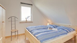 A bedroom with a sloped ceiling, a bed with a blue-striped bedspread, a wooden chair, a ladder, and a window with a view. - Holiday Home "Haus Münster Apartment 2" with Sea View, Private Garden and Wi-Fi (Wohlenberg)
