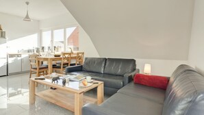 A modern living room with a sofa, coffee table, and dining area. - Holiday Home "Haus Münster Apartment 2" with Sea View, Private Garden and Wi-Fi (Wohlenberg)