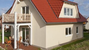 A two-story house with a red-tiled roof, a balcony with a white railing, and a small patio area with outdoor furniture. - Holiday Home "Haus Münster Apartment 2" with Sea View, Private Garden and Wi-Fi (Wohlenberg)