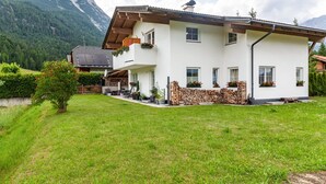 Ein zweistöckiges Haus mit Blick auf die Berge, einer Holzterrasse und einer Steinsäule.