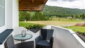 Ein Balkon mit Tisch und Stühlen, Blick auf einen bewaldeten Berg und eine ländliche Landschaft.