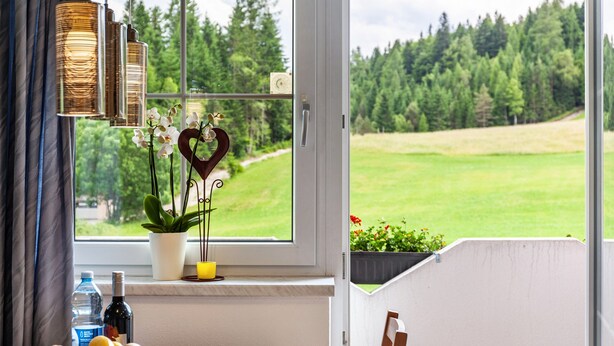 Ein Essbereich mit Tisch, einer Topfpflanze, einer herzförmigen Dekoration und einem Fenster mit Blick auf eine grüne Landschaft.