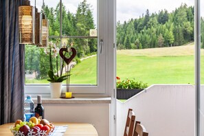 A dining area with a table, a potted plant, a heart-shaped decoration, and a window with a view of a green landscape.