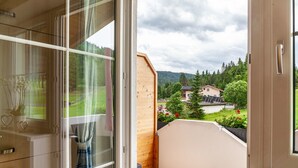 A balcony with a wooden railing, a glass door, and a view of a residential area with houses and trees. - Apartment "Bellamontes Apartment Top 2" with Mountain View, Balcony & Wi-Fi (Leutasch)