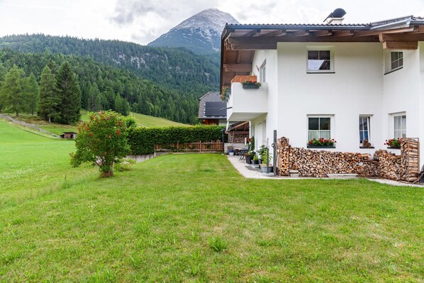 Un bâtiment blanc doté d’un balcon, avec une montagne en arrière-plan et une pelouse bien entretenue.