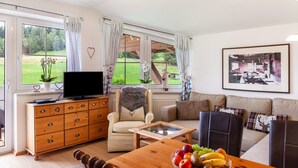 A living room with a sofa, armchairs, a coffee table, a TV on a wooden cabinet, and a large window with curtains. - Apartment "Bellamontes Apartment Top 2" with Mountain View, Balcony & Wi-Fi (Leutasch)