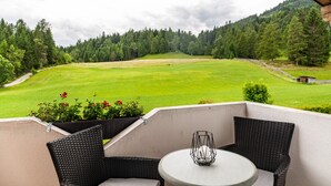 A balcony with wicker furniture, a table, and a view of a green field and forest. - Apartment "Bellamontes Apartment Top 2" with Mountain View, Balcony & Wi-Fi (Leutasch)