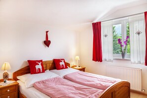 Une chambre à coucher avec un lit en bois, deux tables de chevet avec des lampes, une décoration en forme de cœur rouge et une fenêtre avec des rideaux rouges.