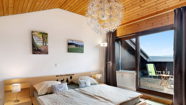 A bedroom with a large bed, a nightstand, a wall-mounted lamp, and a view of the outdoors through a sliding glass door. - Apartment 'Klug' with Mountain View, Private Terrace and Wi-Fi (Schonach im Schwarzwald)