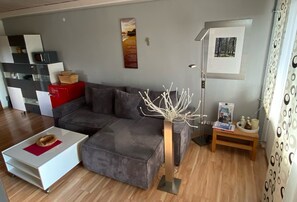 A modern living room with a sectional sofa, a white coffee table, a decorative vase, and a small wooden side table. - Apartment 'Klug' with Mountain View, Private Terrace and Wi-Fi (Schonach im Schwarzwald)